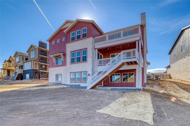 view of front facade featuring a balcony, brick siding, stairway, board and batten siding, and a chimney