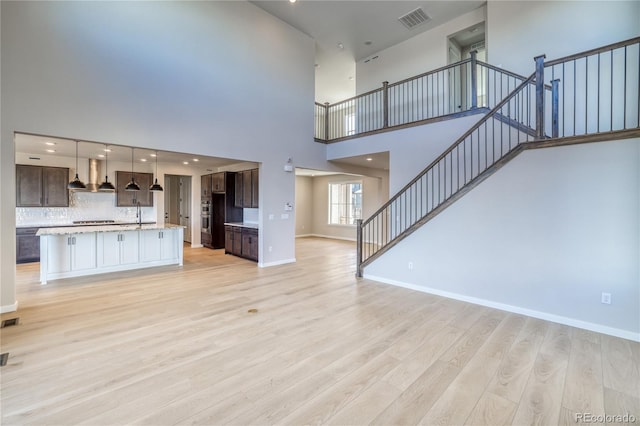 unfurnished living room with light wood-style flooring, stairway, visible vents, and baseboards