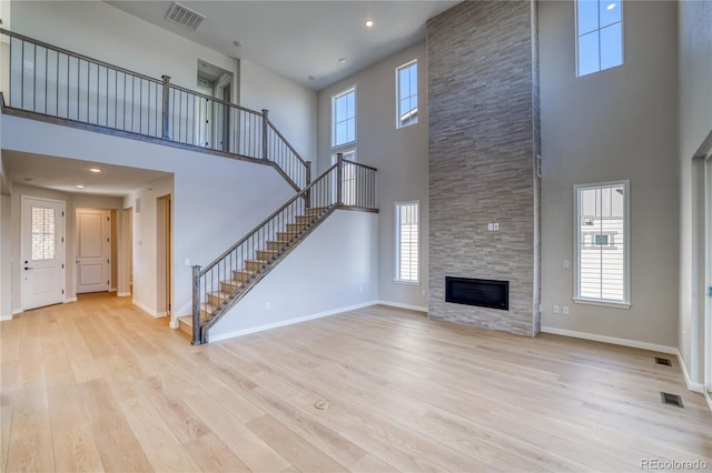 unfurnished living room with a stone fireplace, wood finished floors, visible vents, baseboards, and stairway