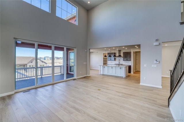 unfurnished living room featuring visible vents, a sink, light wood-type flooring, baseboards, and stairs