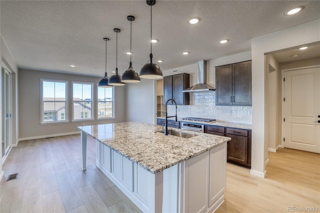 kitchen featuring wall chimney exhaust hood, light wood-type flooring, a sink, and visible vents