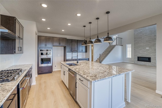 kitchen featuring stainless steel appliances, a sink, light stone countertops, and light wood-style floors