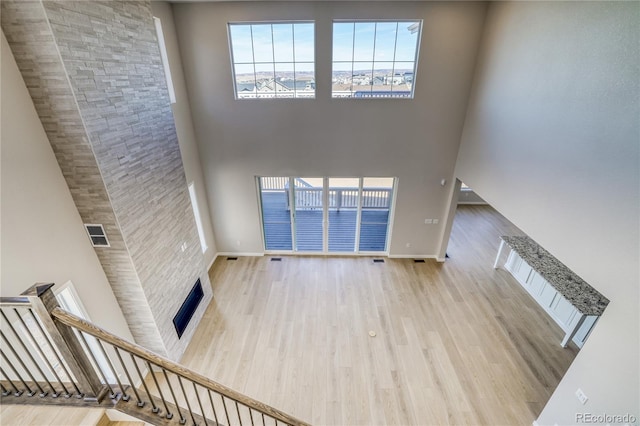 unfurnished living room featuring wood finished floors, visible vents, a towering ceiling, baseboards, and stairway