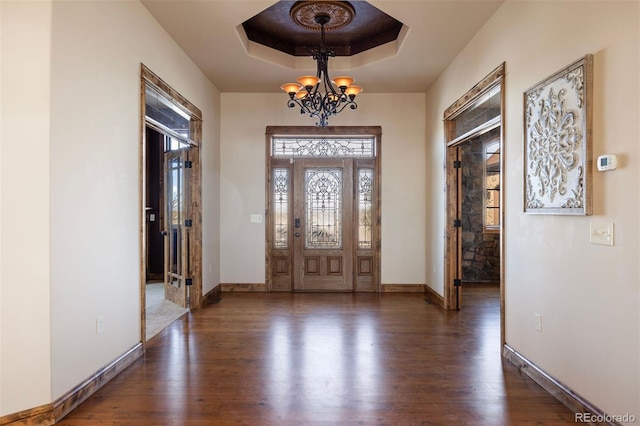 foyer entrance featuring an inviting chandelier, a tray ceiling, and dark hardwood / wood-style flooring