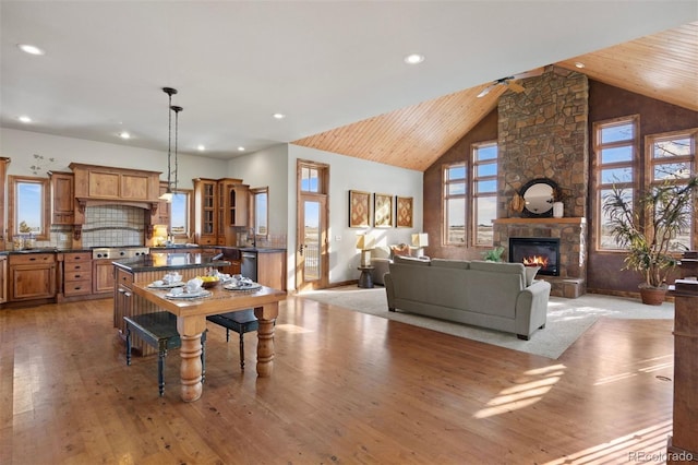 dining room with high vaulted ceiling, a stone fireplace, wooden ceiling, and light wood-type flooring