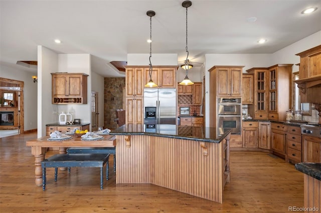 kitchen featuring a breakfast bar, appliances with stainless steel finishes, a kitchen island, pendant lighting, and light hardwood / wood-style floors