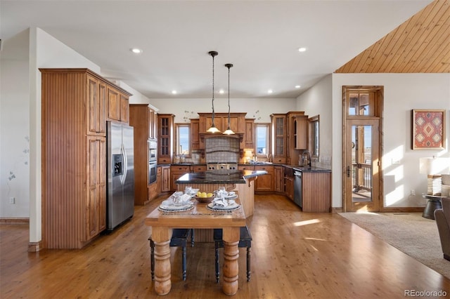 kitchen with light hardwood / wood-style flooring, backsplash, stainless steel appliances, a kitchen island, and decorative light fixtures