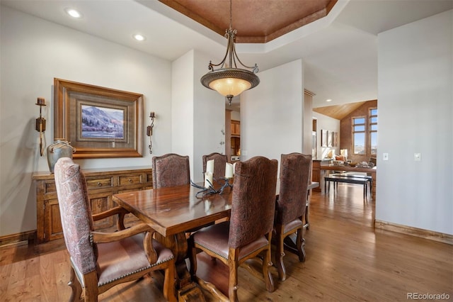 dining area with light wood-type flooring and a tray ceiling