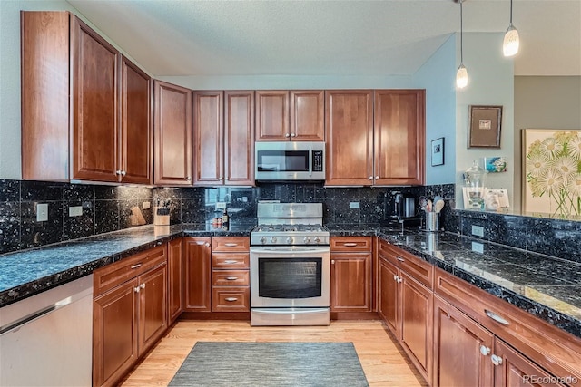 kitchen featuring backsplash, light wood-style flooring, stainless steel appliances, and decorative light fixtures