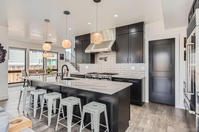 1655 Wolff St, Denver, CO 80204 - kitchen featuring a sink, wall chimney range hood, light stone countertops, backsplash, and light wood-type flooring