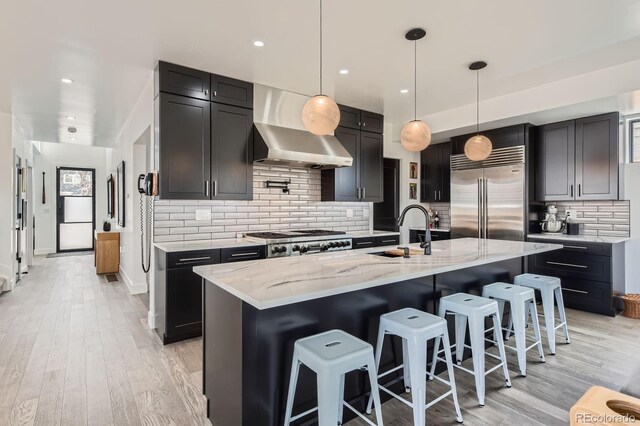 1655 Wolff St, Denver, CO 80204 - kitchen featuring stainless steel appliances, wall chimney range hood, light stone countertops, light wood-style flooring, and recessed lighting