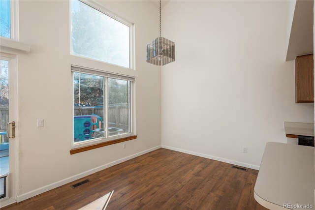 unfurnished dining area featuring a towering ceiling, dark hardwood / wood-style flooring, and a chandelier