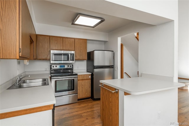 kitchen with appliances with stainless steel finishes, dark hardwood / wood-style flooring, kitchen peninsula, and sink