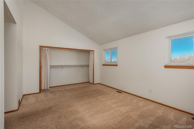 unfurnished bedroom with multiple windows, vaulted ceiling, light colored carpet, and a closet