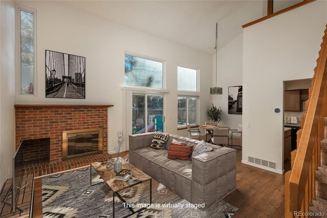 living room featuring a towering ceiling, dark hardwood / wood-style flooring, and a brick fireplace