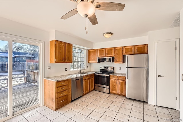 kitchen featuring light tile patterned flooring, sink, light stone counters, appliances with stainless steel finishes, and ceiling fan