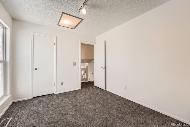 unfurnished bedroom featuring dark colored carpet, track lighting, and a textured ceiling