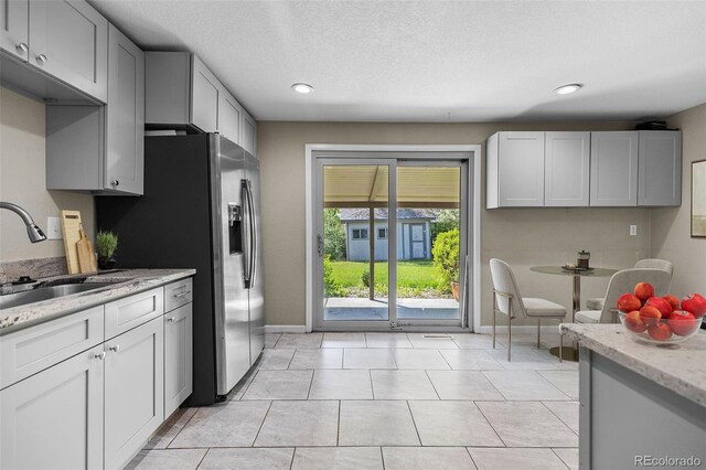 8305 Eaton Way, Arvada, CO 80003 - kitchen with a sink, light stone counters, baseboards, recessed lighting, and stainless steel fridge