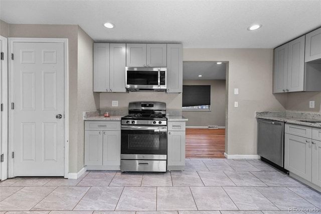 8305 Eaton Way, Arvada, CO 80003 - kitchen with stainless steel appliances, gray cabinetry, baseboards, light stone counters, and recessed lighting