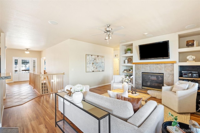 living room featuring a tiled fireplace, built in shelves, light hardwood / wood-style floors, and ceiling fan