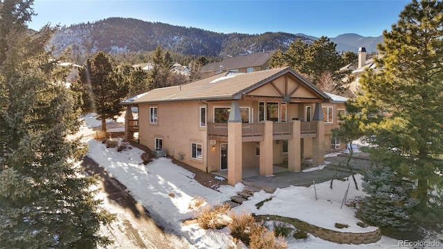 snow covered rear of property featuring a balcony and a mountain view