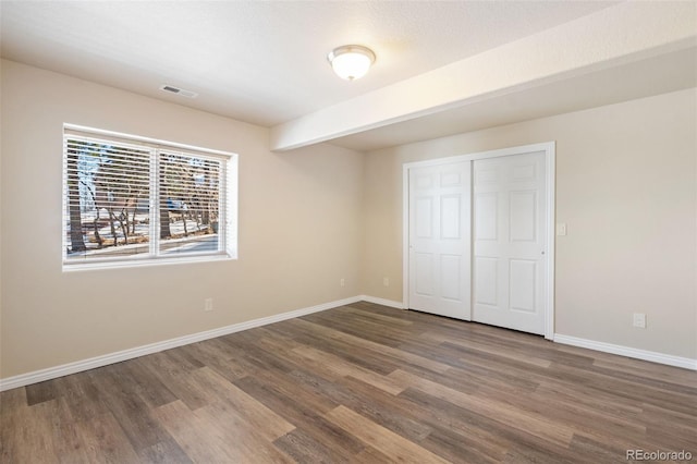 unfurnished bedroom featuring dark wood-type flooring, a textured ceiling, beam ceiling, and a closet