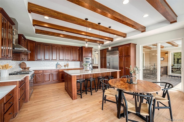 kitchen with high end appliances, tasteful backsplash, a center island, light wood-type flooring, and wall chimney range hood