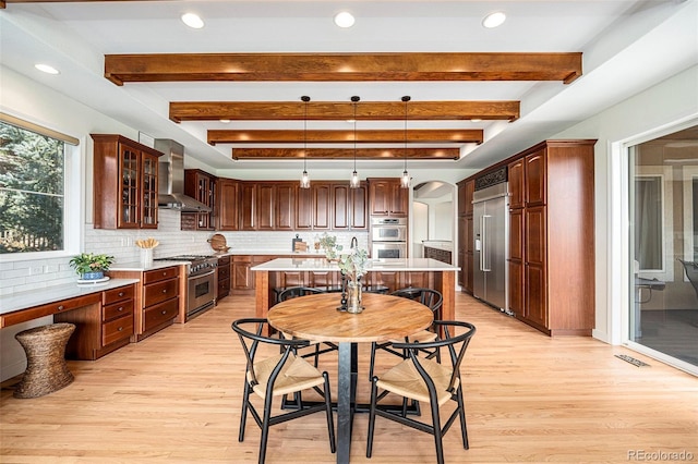 kitchen with pendant lighting, wall chimney range hood, backsplash, high end appliances, and a kitchen island