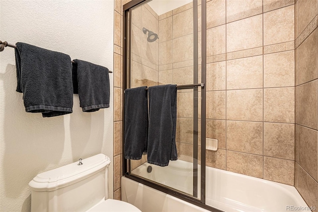 bathroom featuring toilet and shower / bath combination with glass door