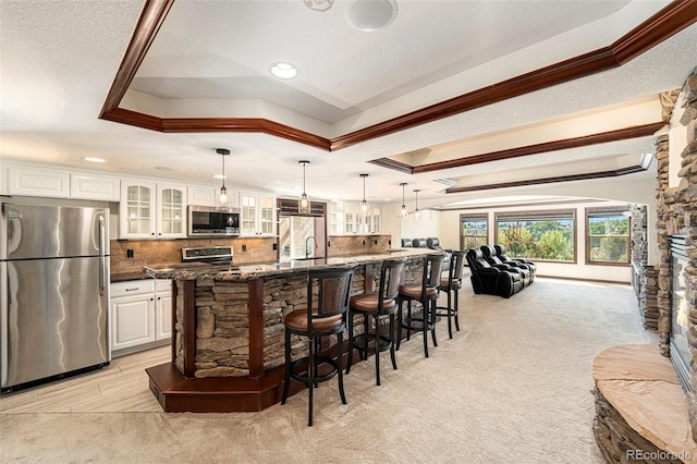 kitchen featuring white cabinetry, appliances with stainless steel finishes, a tray ceiling, and a large island with sink