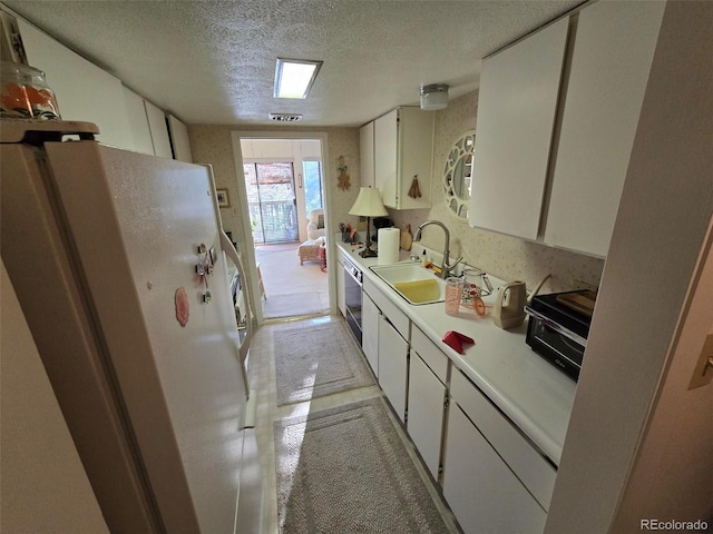 kitchen featuring a textured ceiling, a sink, visible vents, light countertops, and freestanding refrigerator