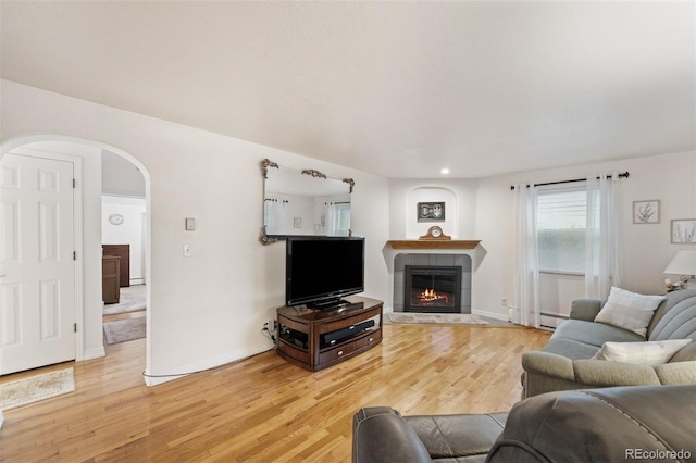 3888 Estes St, Wheat Ridge, CO 80033 - living room featuring arched walkways, light wood-type flooring, a tile fireplace, a baseboard heating unit, and recessed lighting