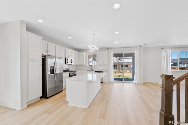 kitchen with appliances with stainless steel finishes, a sink, light countertops, white cabinets, and light wood finished floors