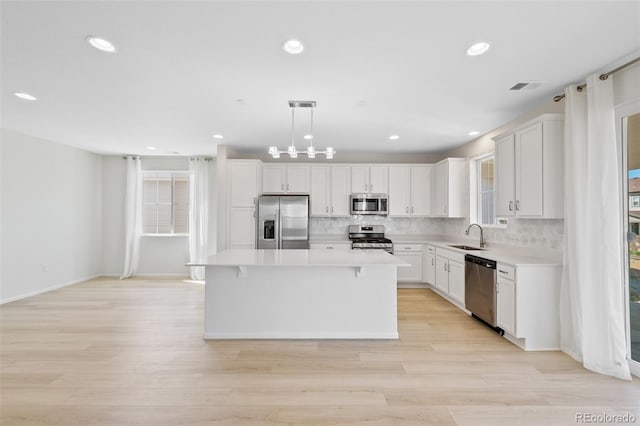 kitchen with appliances with stainless steel finishes, a center island, light countertops, light wood finished floors, and recessed lighting