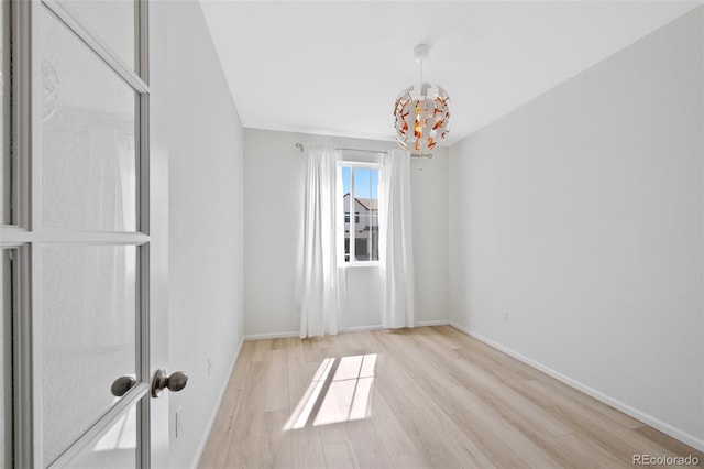empty room with wood finished floors, a chandelier, and baseboards