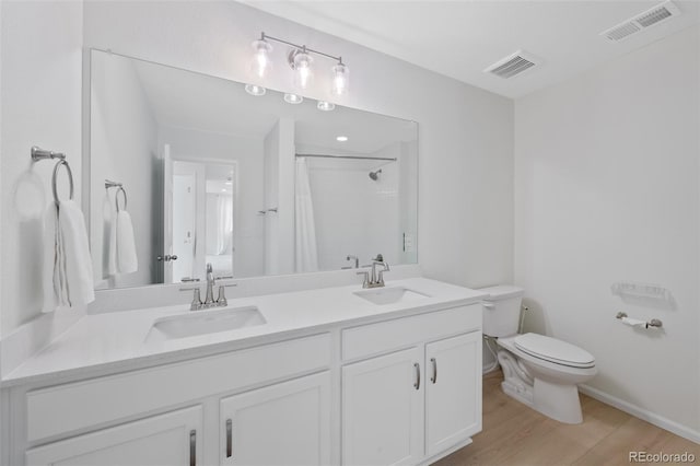 bathroom with toilet, wood finished floors, a shower with shower curtain, double vanity, and baseboards