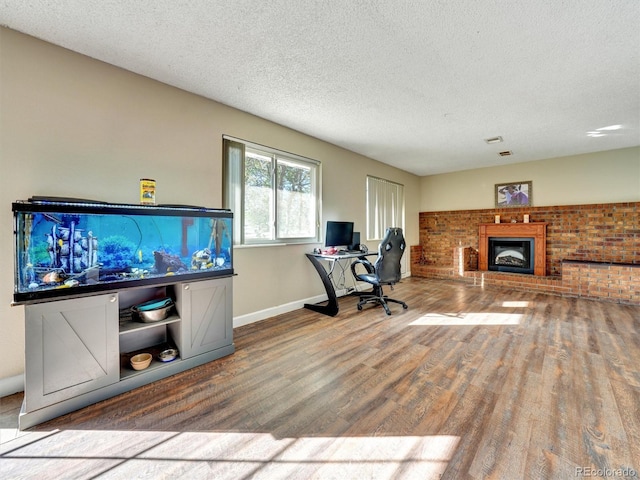 office space with a brick fireplace, a textured ceiling, baseboards, and wood finished floors