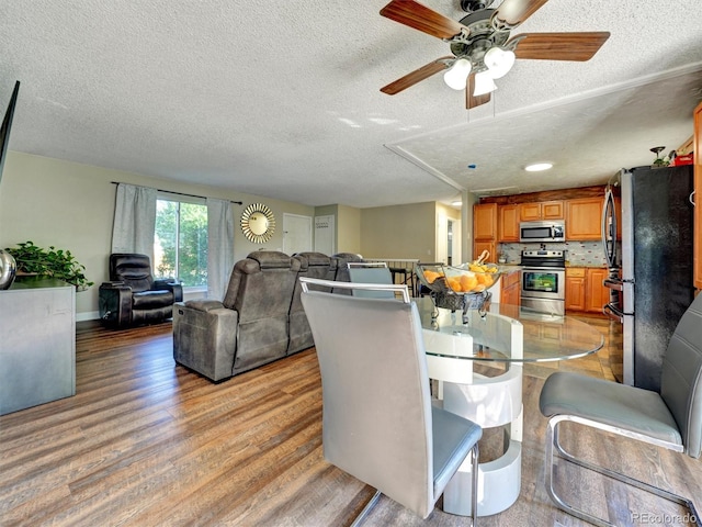 dining space featuring light wood-type flooring, a textured ceiling, ceiling fan, and baseboards