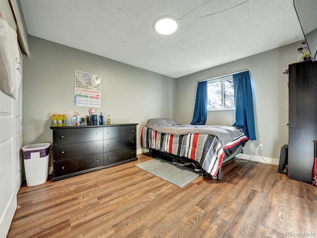 bedroom featuring a textured ceiling, baseboards, and wood finished floors