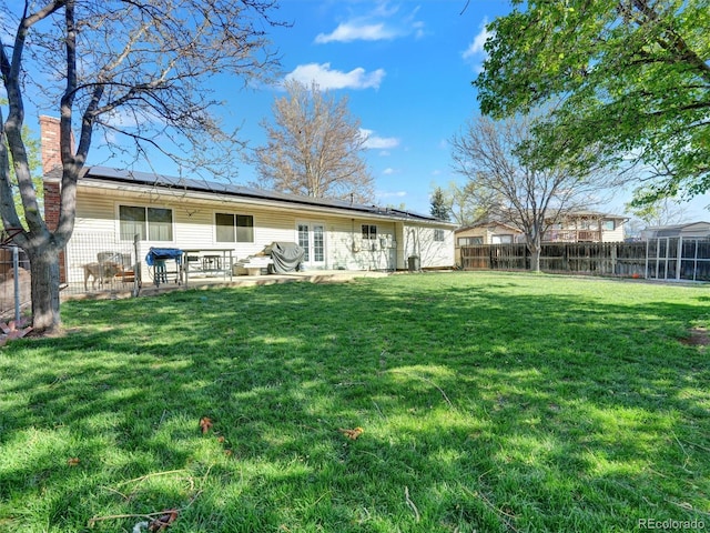 rear view of property featuring a lawn, a patio, solar panels, and a chimney