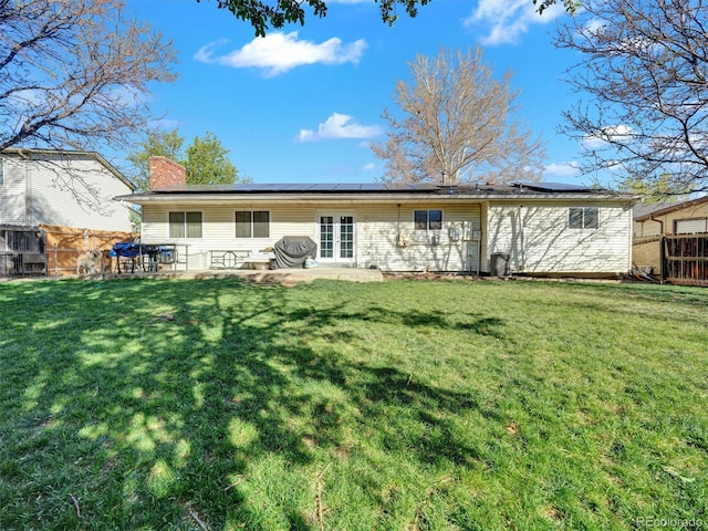 back of property with roof mounted solar panels, a chimney, a lawn, and french doors
