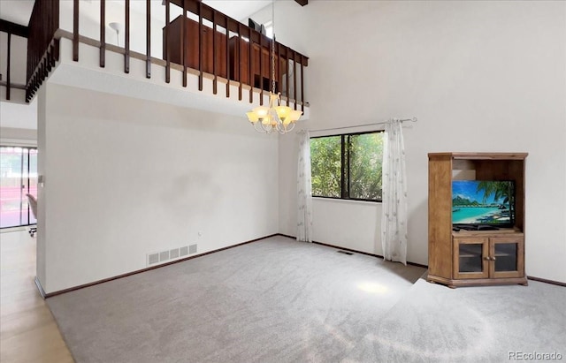 unfurnished living room featuring carpet floors, a chandelier, baseboards, a towering ceiling, and visible vents