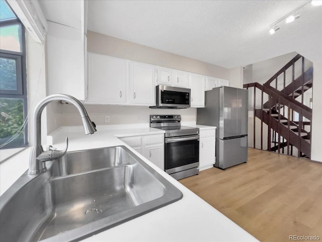 kitchen featuring light wood-type flooring, light countertops, white cabinets, a sink, and stainless steel appliances