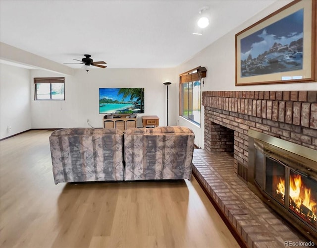 living area with baseboards, a brick fireplace, wood finished floors, and ceiling fan