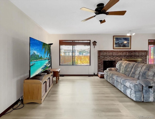 living room with light wood-style floors, baseboards, a fireplace, and a ceiling fan