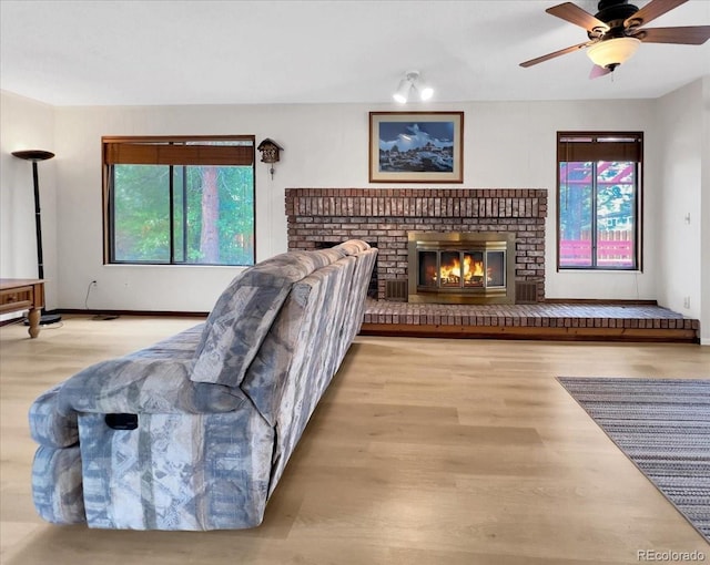living area featuring baseboards, ceiling fan, a brick fireplace, and wood finished floors
