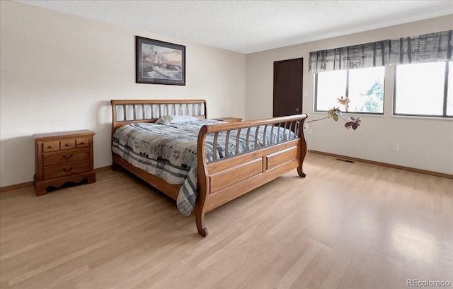 bedroom with baseboards, a textured ceiling, and light wood-style flooring