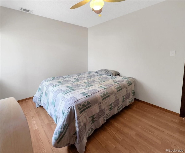 bedroom featuring ceiling fan, baseboards, visible vents, and wood finished floors