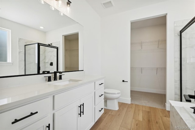 bathroom featuring a spacious closet, a shower stall, vanity, and wood finished floors