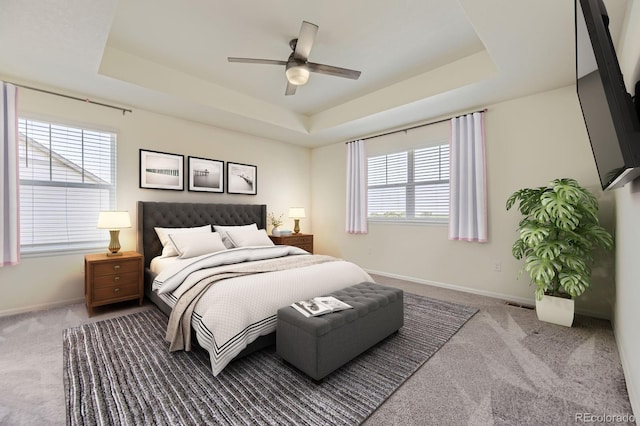 carpeted bedroom featuring visible vents, baseboards, a tray ceiling, and a ceiling fan